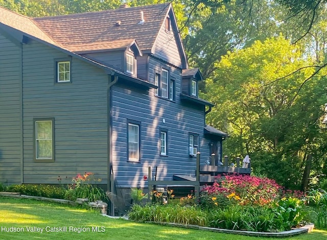 view of home's exterior with a shingled roof, a lawn, and a deck