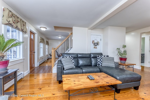 living room featuring a baseboard radiator, baseboards, stairway, and light wood finished floors