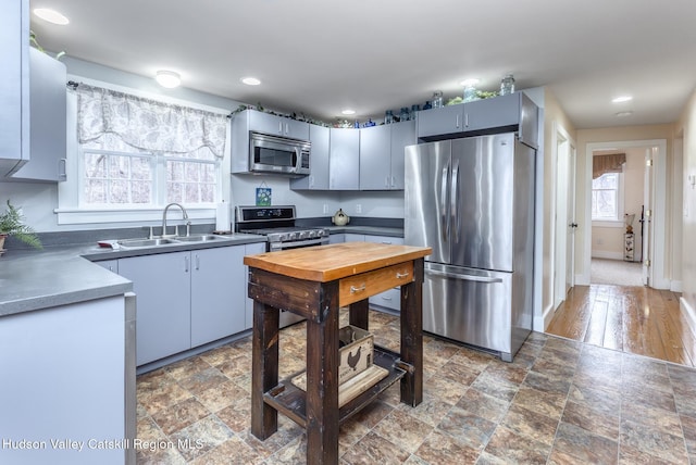 kitchen with recessed lighting, appliances with stainless steel finishes, stone finish floor, a sink, and baseboards