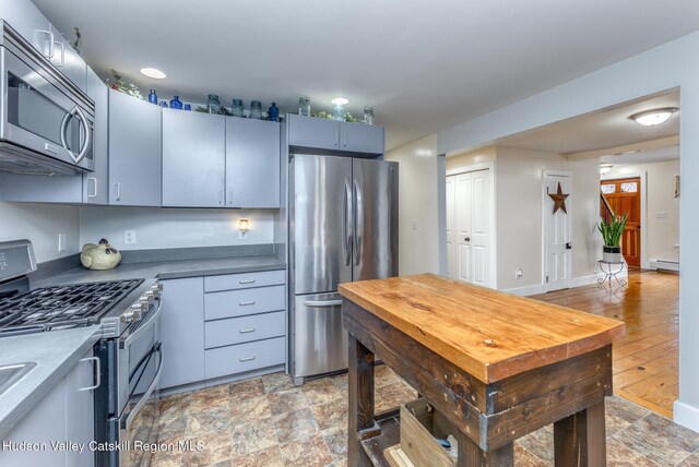 kitchen with a baseboard heating unit, stainless steel appliances, stone finish floor, and baseboards