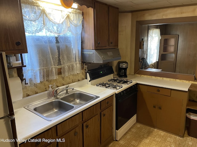 kitchen with wooden walls, white gas stove, extractor fan, and sink