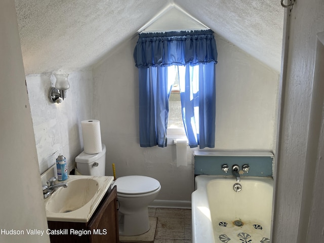 bathroom with a washtub, a textured ceiling, lofted ceiling, toilet, and vanity