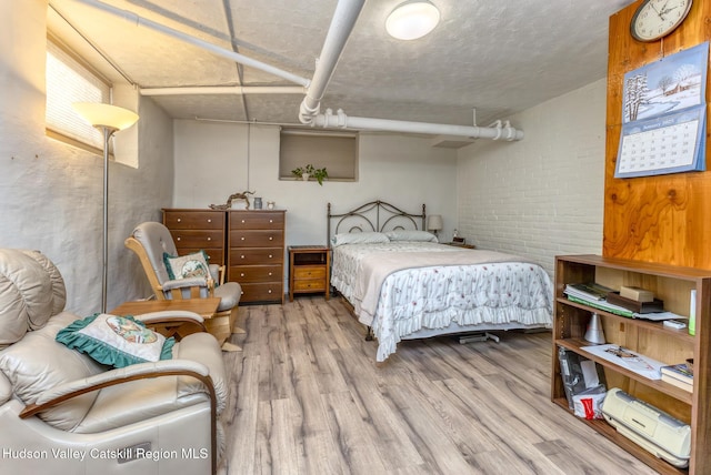 bedroom featuring brick wall and light wood-type flooring