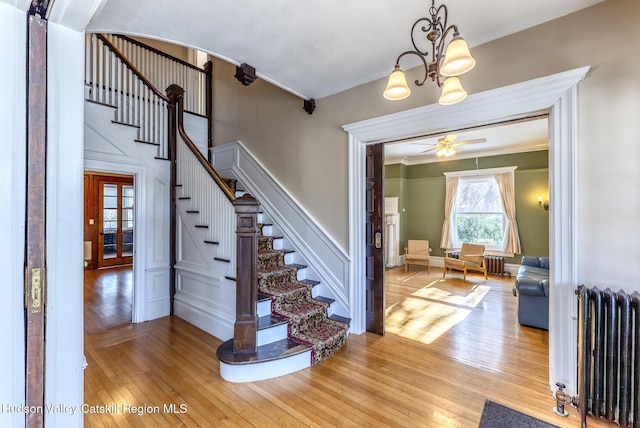 staircase featuring crown molding, hardwood / wood-style flooring, radiator heating unit, and ceiling fan with notable chandelier