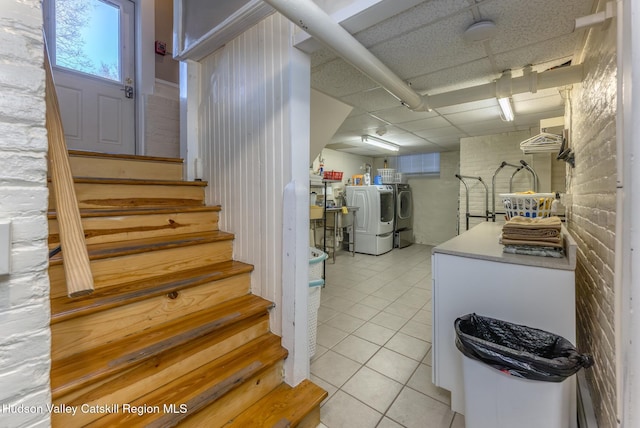 interior space with a drop ceiling, light tile patterned floors, independent washer and dryer, and white cabinets