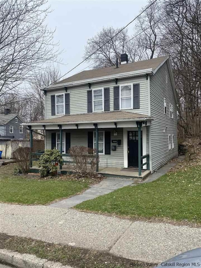 view of front of house with covered porch, a front lawn, and a chimney