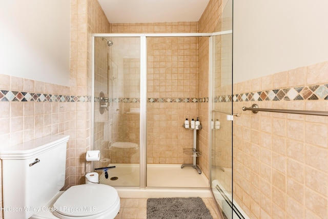 bathroom with toilet, a stall shower, tile walls, wainscoting, and tile patterned flooring