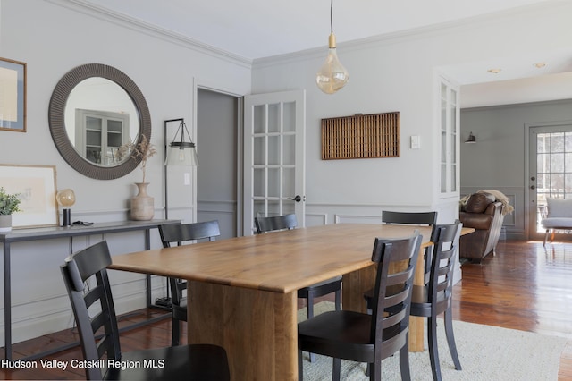 dining area featuring dark wood-style floors, a wainscoted wall, a decorative wall, and crown molding