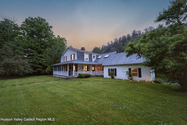 rear view of property featuring a yard, a gambrel roof, a porch, and a chimney