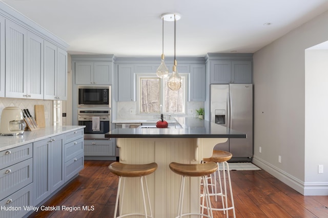 kitchen with baseboards, dark wood-style flooring, appliances with stainless steel finishes, a kitchen breakfast bar, and backsplash