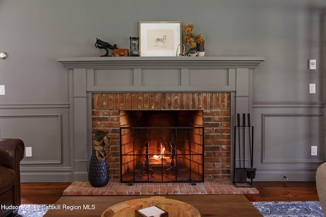 interior details with a decorative wall, wainscoting, a brick fireplace, and wood finished floors