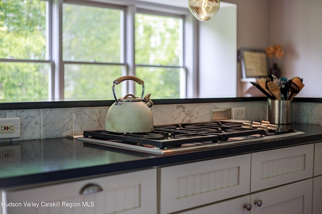 interior details with dark countertops, decorative backsplash, white cabinets, and stainless steel gas stovetop