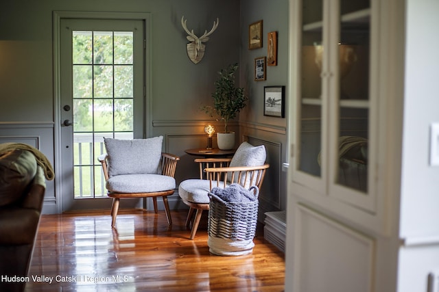 sitting room featuring a decorative wall, wood finished floors, and wainscoting