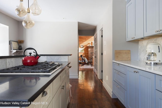 kitchen with backsplash, light stone countertops, stainless steel gas cooktop, hanging light fixtures, and dark wood-style flooring