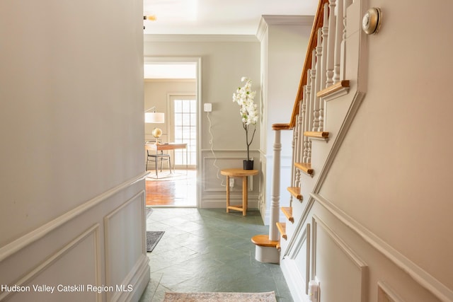 hall with a decorative wall, ornamental molding, stairway, and a wainscoted wall