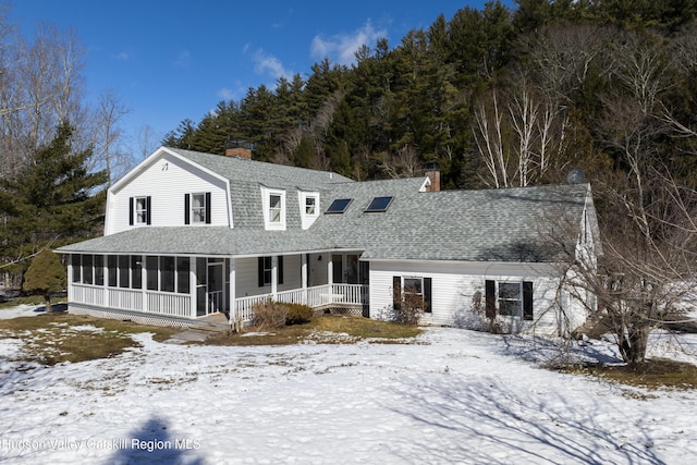 view of front of house with roof with shingles, a chimney, and a sunroom