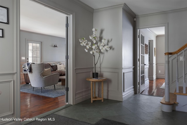 corridor featuring crown molding, stairway, wainscoting, wood finished floors, and a decorative wall