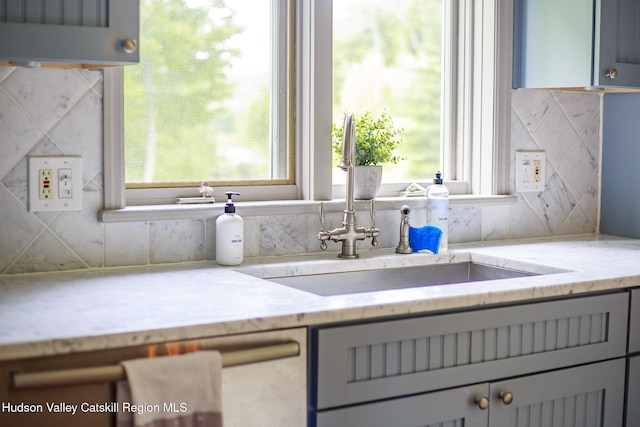 kitchen featuring a sink, backsplash, gray cabinetry, and light stone countertops