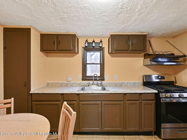 kitchen featuring wall chimney exhaust hood, gas range, a textured ceiling, sink, and light tile patterned floors