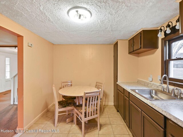 kitchen featuring a textured ceiling, dark brown cabinets, light tile patterned floors, and sink