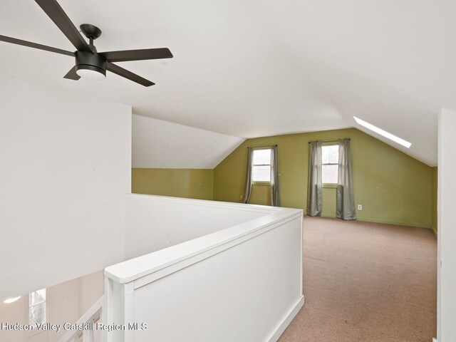 additional living space featuring light carpet, ceiling fan, and vaulted ceiling with skylight