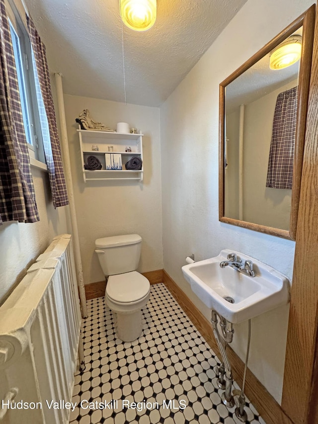 bathroom featuring toilet, a textured ceiling, baseboards, and a sink