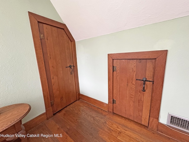 hallway with baseboards, visible vents, vaulted ceiling, and wood finished floors