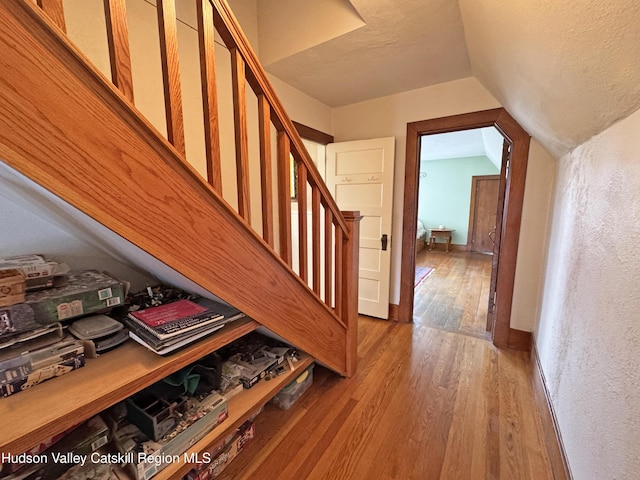 staircase featuring vaulted ceiling, a textured ceiling, wood finished floors, and baseboards