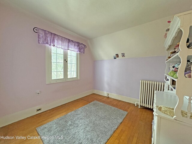 bedroom featuring lofted ceiling, radiator, wood-type flooring, and baseboards