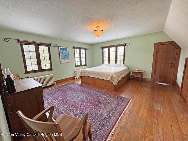 bedroom with baseboards, hardwood / wood-style flooring, radiator heating unit, vaulted ceiling, and a textured ceiling