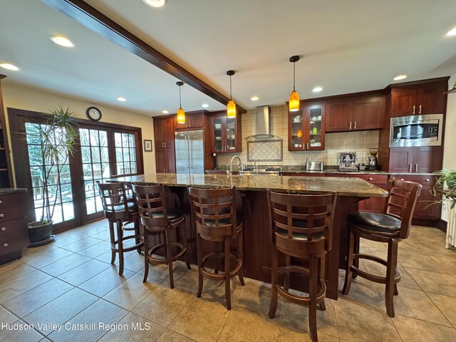 kitchen with tasteful backsplash, glass insert cabinets, built in appliances, wall chimney range hood, and recessed lighting