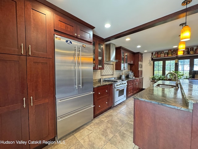 kitchen featuring decorative backsplash, high end appliances, glass insert cabinets, wall chimney range hood, and a sink