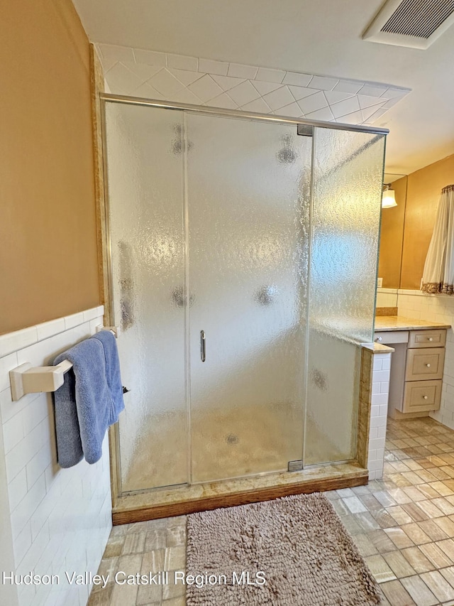 full bathroom featuring tile walls, visible vents, a shower stall, and vanity