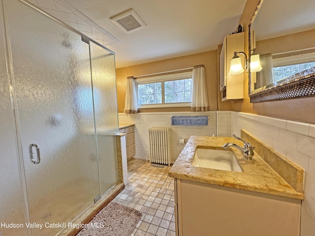 bathroom with radiator heating unit, tile walls, vanity, a stall shower, and wainscoting