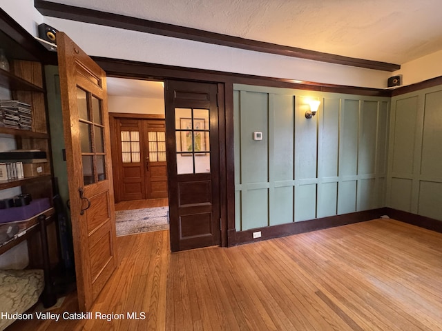 entrance foyer with wood-type flooring, a decorative wall, a textured ceiling, and french doors