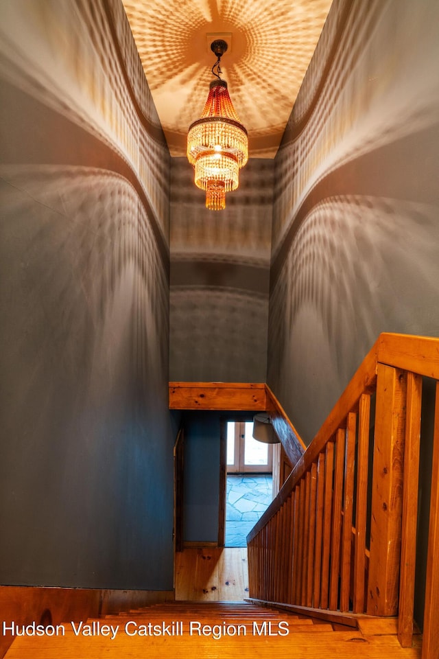 stairway featuring wood finished floors, a towering ceiling, and a chandelier