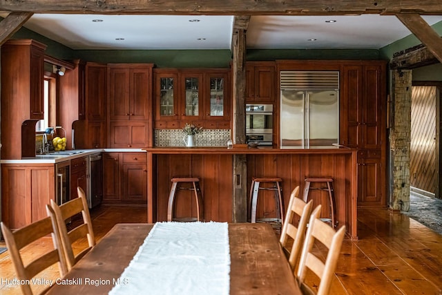 kitchen with glass insert cabinets, wood finished floors, brown cabinetry, stainless steel appliances, and a sink