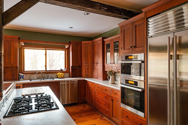 kitchen with beamed ceiling, a sink, stainless steel appliances, light wood finished floors, and light countertops