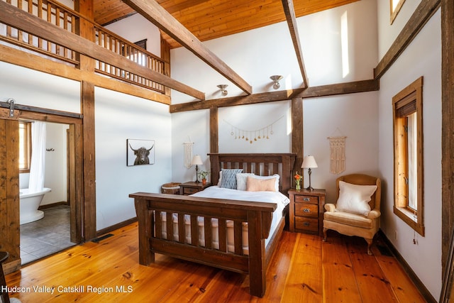 bedroom featuring hardwood / wood-style floors, a barn door, baseboards, and high vaulted ceiling