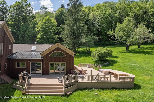 back of property with a wooden deck, a lawn, metal roof, and a standing seam roof