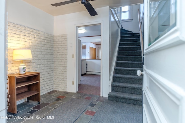 stairway with ceiling fan, a baseboard radiator, and brick wall