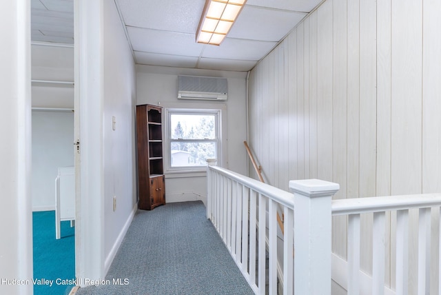 hall featuring carpet floors, a wall unit AC, and a paneled ceiling