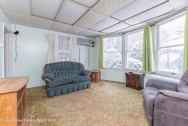 living area with an AC wall unit, carpet floors, and a drop ceiling