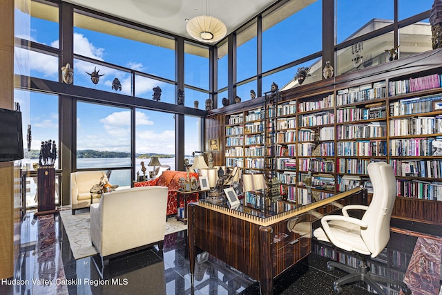 office area featuring a towering ceiling, a water view, and a wall of windows