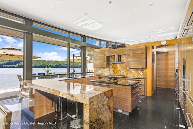 kitchen with backsplash, a water view, wall chimney range hood, sink, and a kitchen island