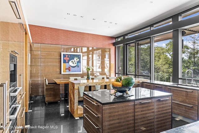 interior space with wall oven, a center island, dark brown cabinets, and sink