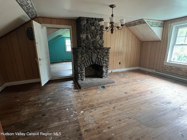 unfurnished living room featuring hardwood / wood-style floors, vaulted ceiling, a stone fireplace, and wood walls