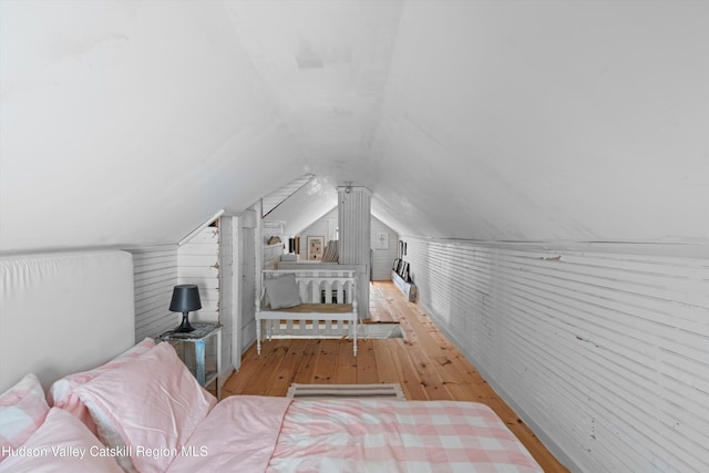 bedroom featuring light hardwood / wood-style flooring, wood walls, and vaulted ceiling