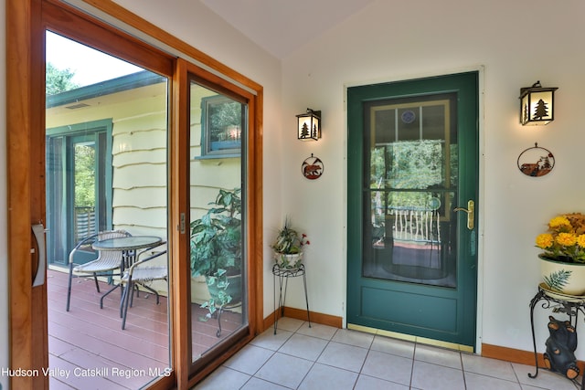 doorway to outside with light tile patterned floors and vaulted ceiling