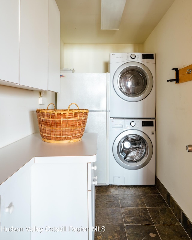 clothes washing area featuring stacked washer / drying machine, cabinet space, and baseboards